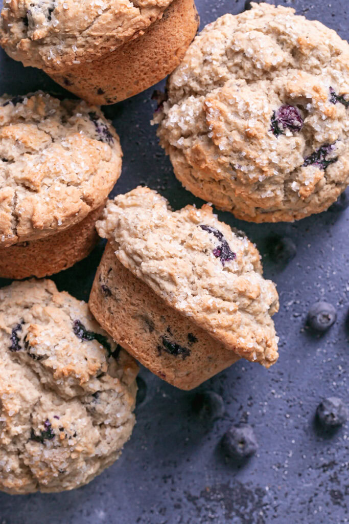 blueberry muffins on a blueberry colored backdrop with fresh blueberries around the muffins
