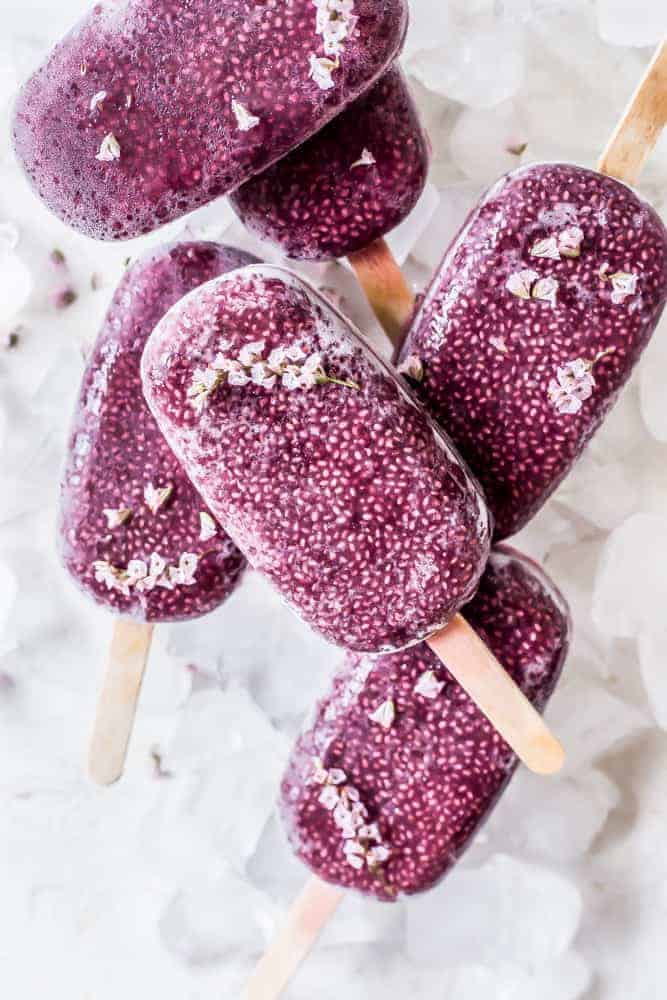purple coconut acai chia seed popsicles stacked on top of one another on top of ice cubes.