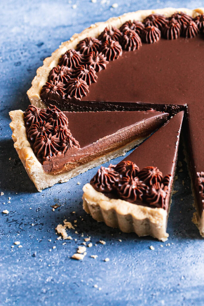 3/4 shot of full twix tart with two slices sliced on a blue backdrop