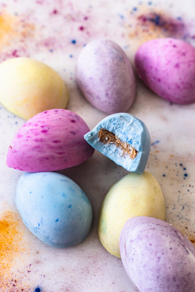 white chocolate colored eggs stacked on top of each other, one with a bite taken out of it to reveal the peanut butter filling