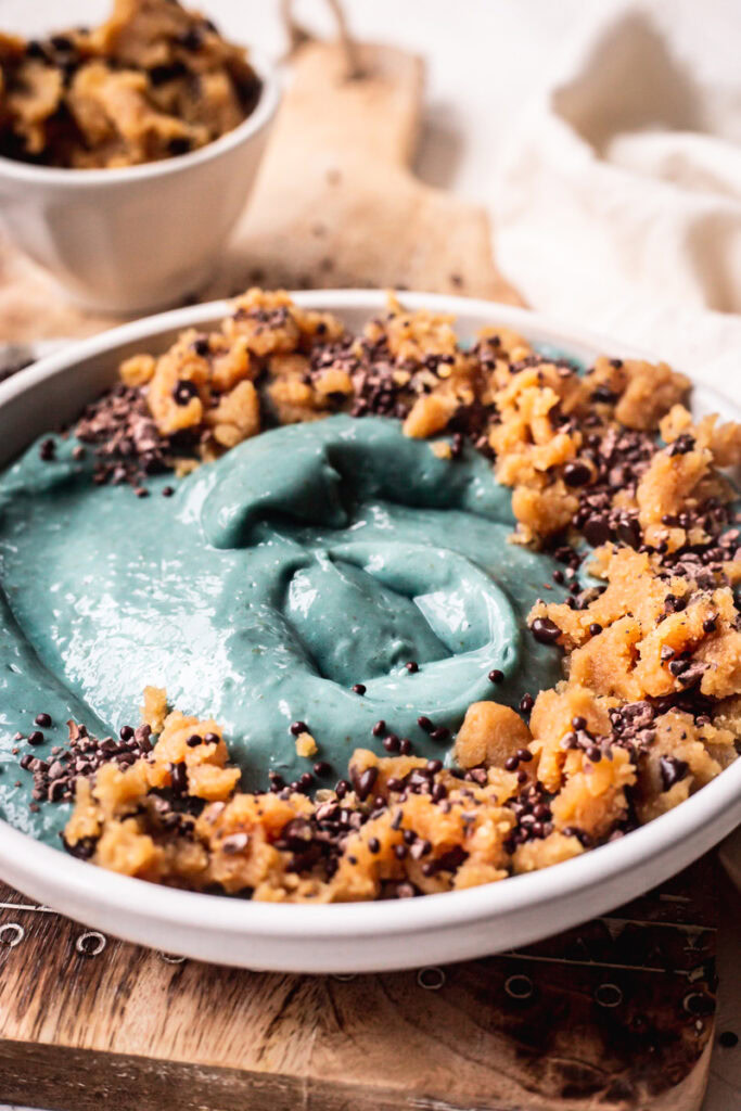 a side view of a blue spirulina smoothie bowl topped with almond flour cookie dough sprinkled with chocolate covered chia seeds.