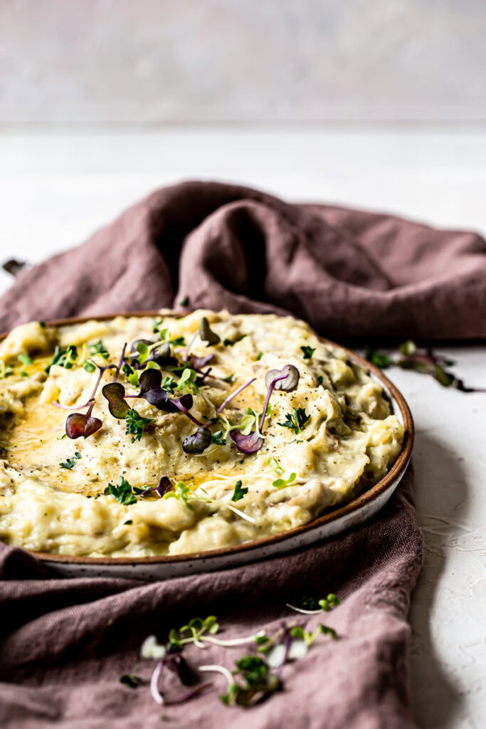 a bowl of mashed potatoes with melted butter garnished with micro greens on top of a purple linen towel
