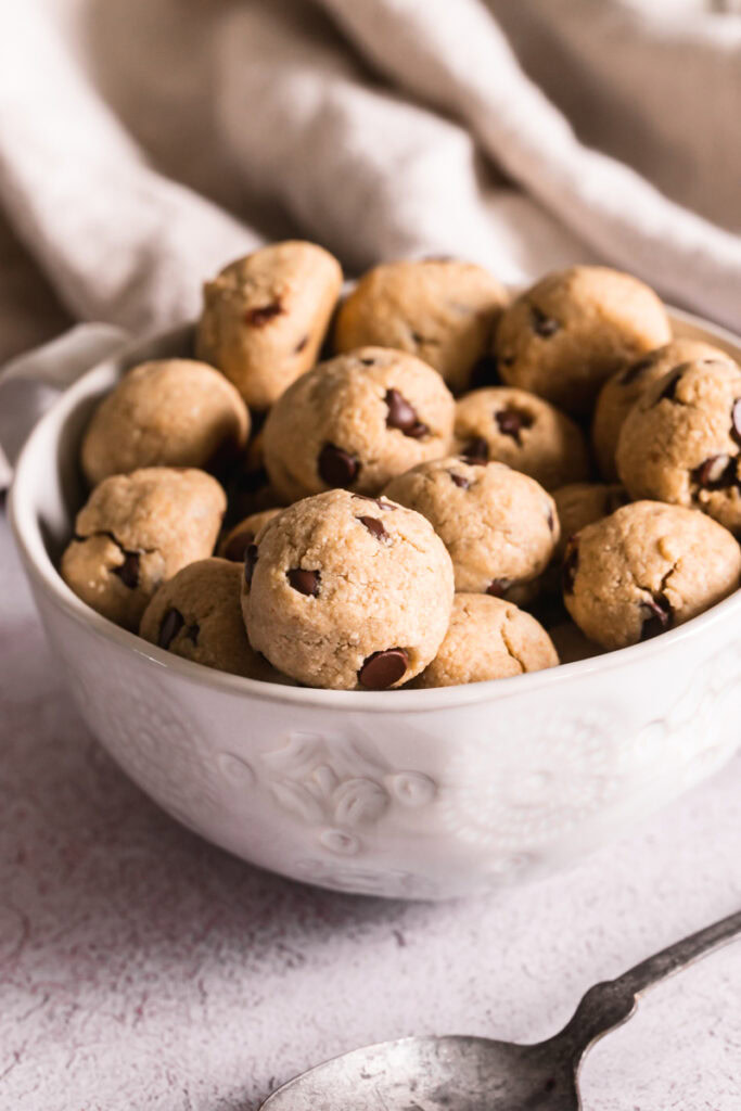 a close up of round balls of cookie crisp cereal in a mug with a spoon beside it.