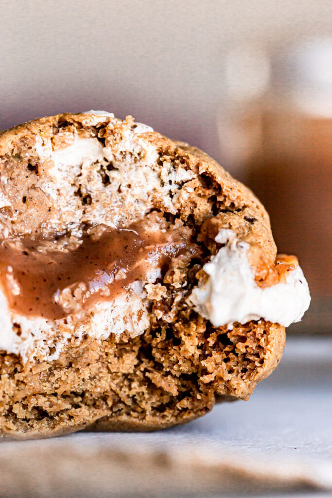 very up close bite shot of an apple butter whoopie pie on a plate with a jar of apple butter blurred in the background