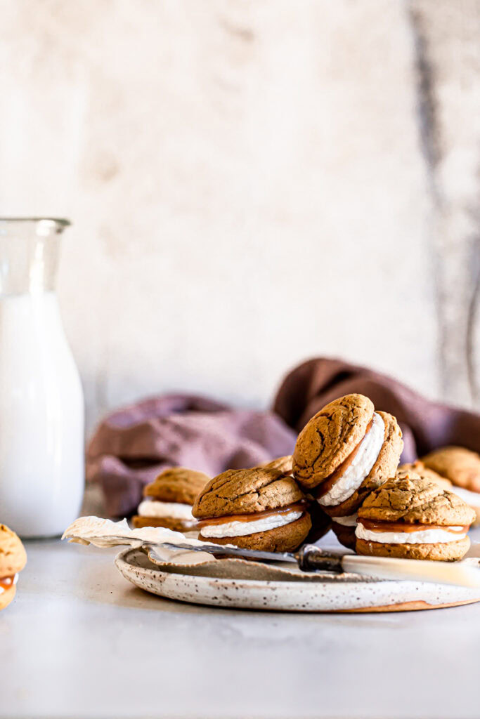 apple butter whoopie pies piled on a plate with a jug of almond milk in the background