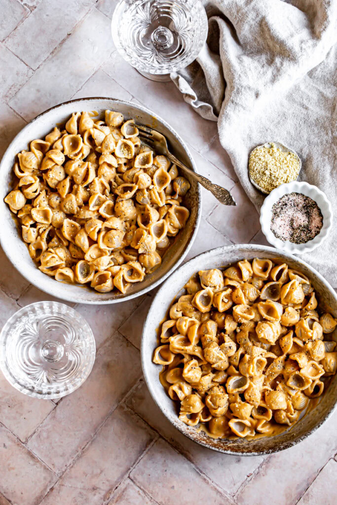 two bowls of Mac and cheese with a linen napkin two glasses of water a bowl of salt and a bowl of vegan parmesan cheese