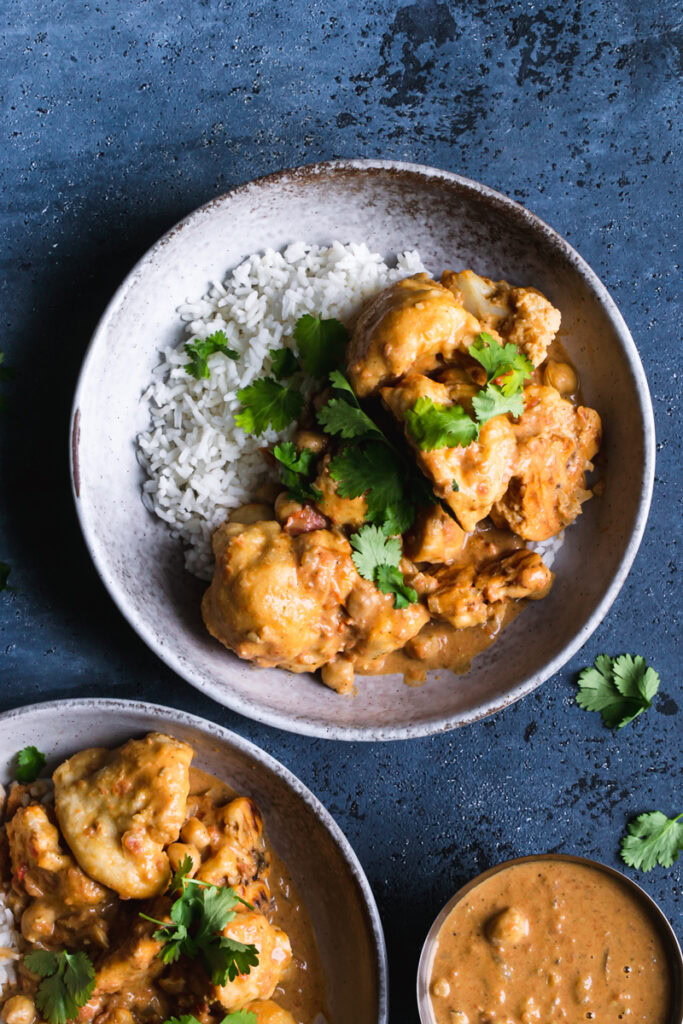 two bowls of rice with breaded cauliflower tossed in a vegan Indian butter sauce garnished with fresh cilantro and a side serving of naan