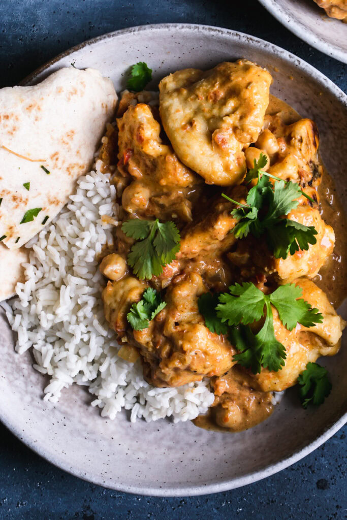 close up shot of a bowl of rice with naan butter cauliflower on top garnished with fresh cilantro leaves and a side of naan bread