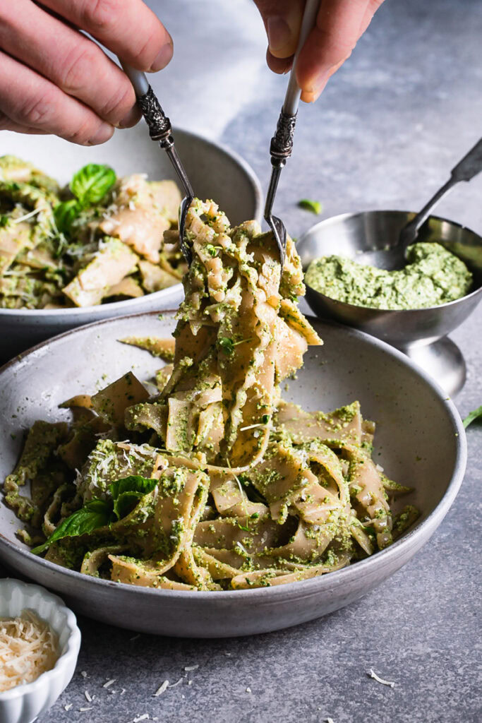 an action shot of two hands holding two forks serving some of the pasta into the bowl