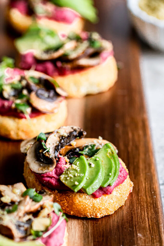 close up of hash browns topped with beet hummus, sliced avocado, balsamic roasted mushrooms, vegan parmesan cheese and micro greens