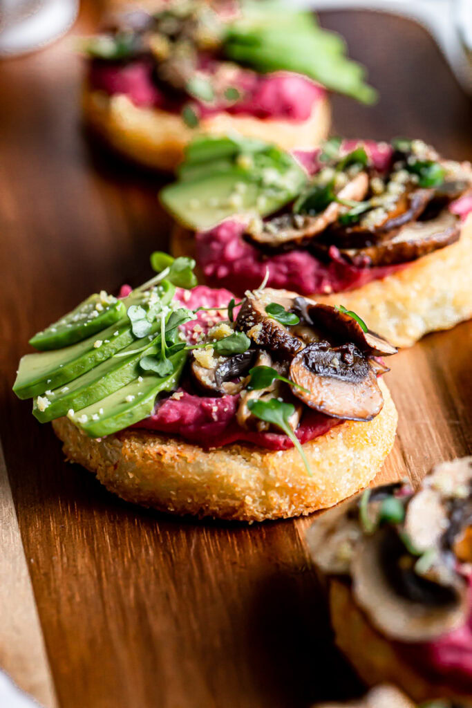close up of hash browns topped with beet hummus, sliced avocado, balsamic roasted mushrooms, vegan parmesan cheese and micro greens