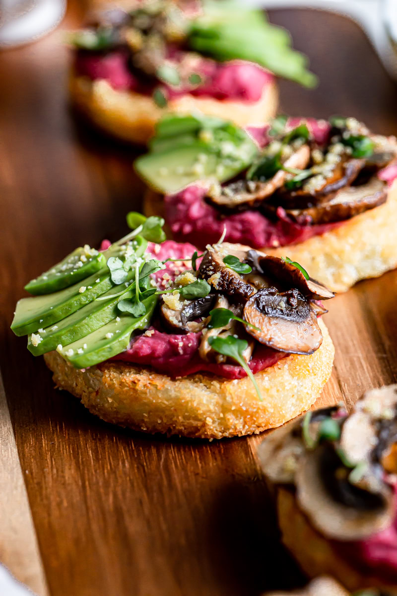 close up of hash browns topped with beet hummus, sliced avocado, balsamic roasted mushrooms, vegan parmesan cheese and micro greens