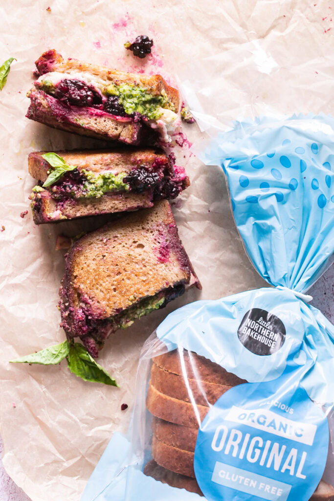 vegan blackberry pesto grilled cheese sandwich halves on a piece of parchment paper with a loaf of little northern bakehouse bread next to it
