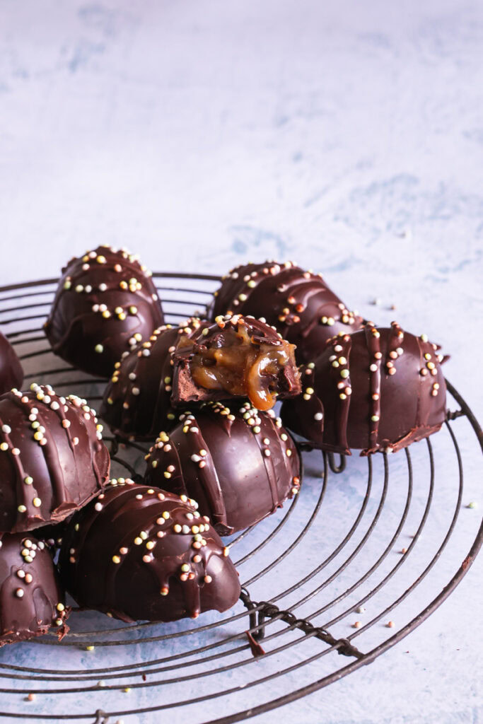 a vertical image of chocolate eggs decorated with sprinkles with one of the eggs bit into to show the caramel filling