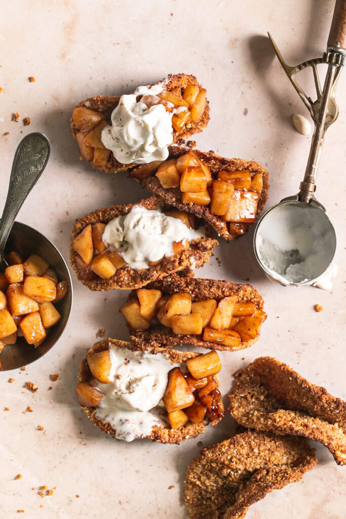 overhead image of apple pie tacos with a bowl of apple filling beside it, two empty baked taco shells and an ice cream scoop