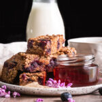 Blueberry Oatmeal French Toast Sticks on a plate with a jar of maple syrup beside it and a cup of coffee and jug of almond milk in the background