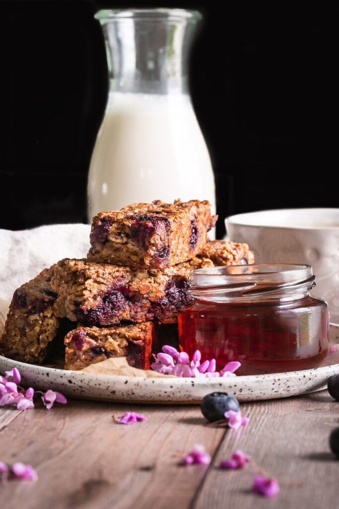 Blueberry Oatmeal French Toast Sticks on a plate with a jar of maple syrup beside it and a cup of coffee and jug of almond milk in the background