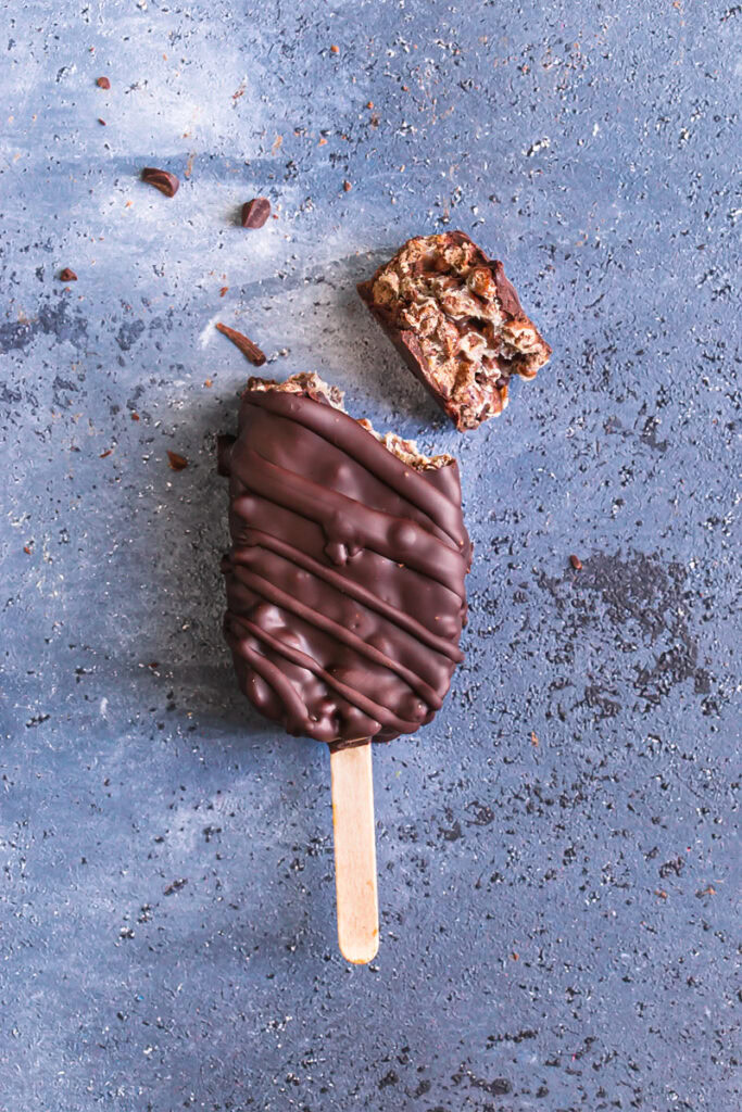 a single chocolate covered cocoa Krispie crunch pop with the top broken off to show the Krispie cereal inside