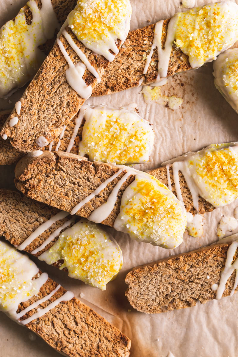 lemon vanilla biscotti piled on top of each other on top of a piece of parchment paper dipped in coconut butter and sprinkled with sparkling sugar and turmeric for color