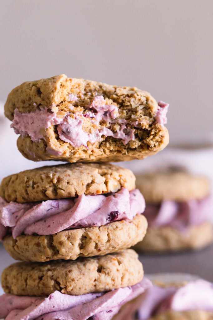 a close up vertical image of stacked blackberry cream sandwich cookies with a bite taken out of the top one