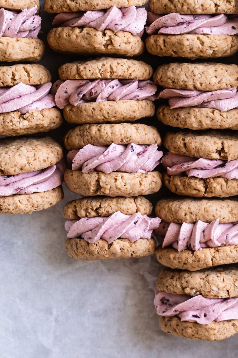 oatmeal sandwich cookies with blackberry cream filling laid in a tray all lined up with the cream filling showing