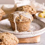 head on shot of lemon poppy seed muffins with one on a plate drizzled with lemon glaze and a bowl of lemons in the background