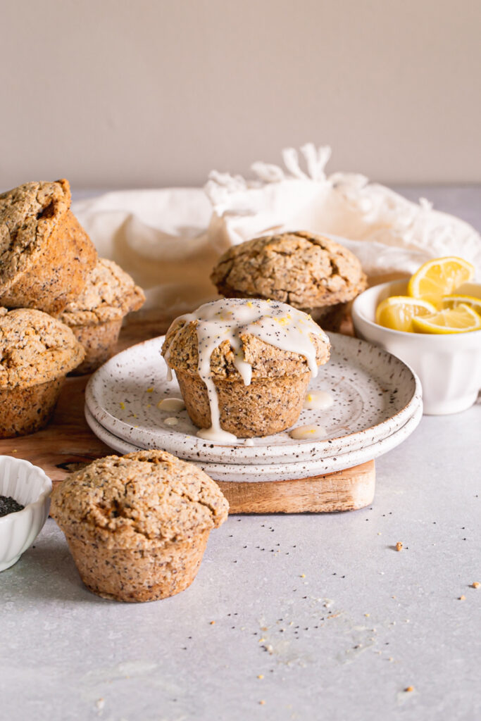 head on shot of lemon poppy seed muffins with one on a plate drizzled with lemon glaze and a bowl of lemons in the background