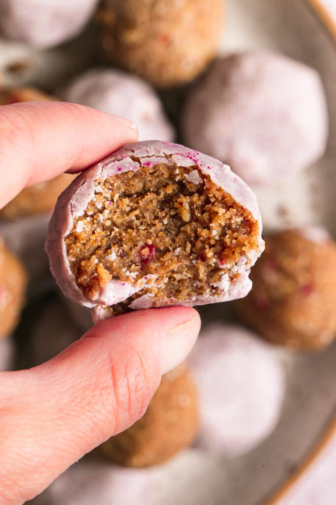 a single strawberries and cream granola bite held in between fingers with a bite taken out of it