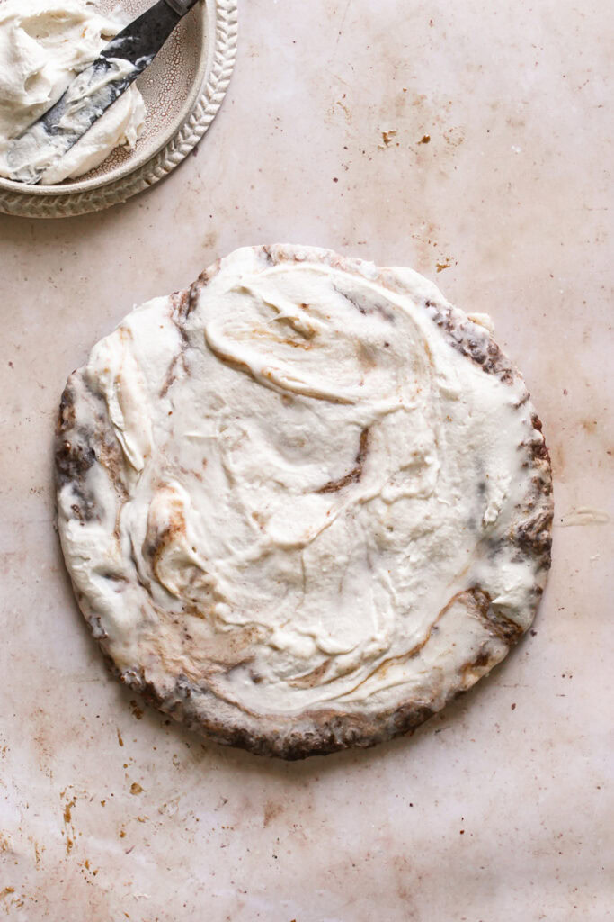 uncut cinnamon roll pizza with a bowl of vegan cream cheese icing in the top left
