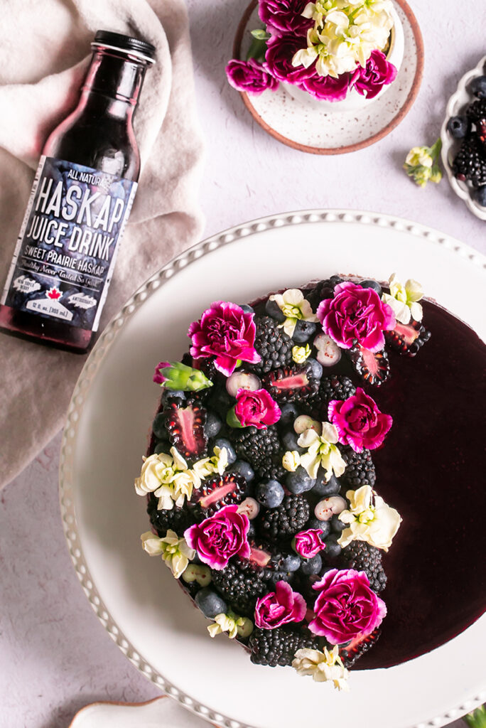 unsliced haskap berry cheesecake on a cake plate with a bottle of haskap berry juice next to it