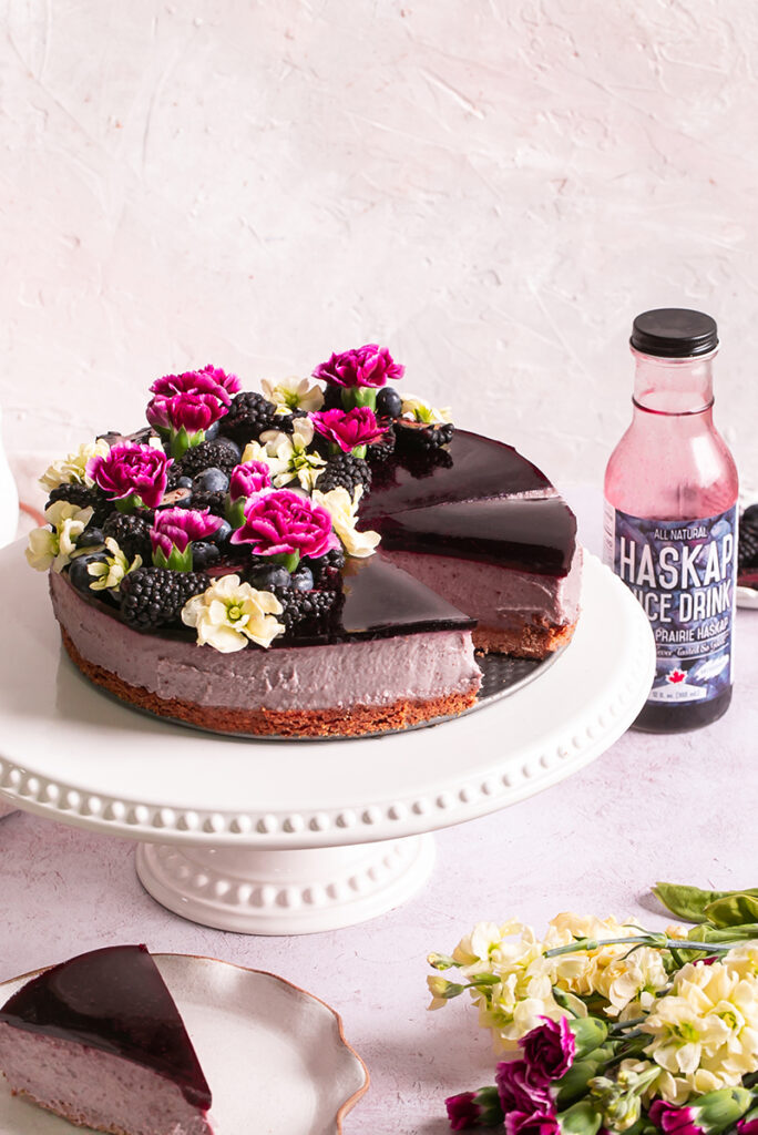 side view of haskap berry cheesecake sliced with a bottle of haskap juice in the background