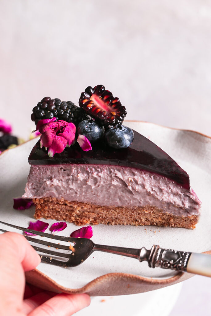 a side view of a slice of haskap berry cheesecake with a fork on a plate