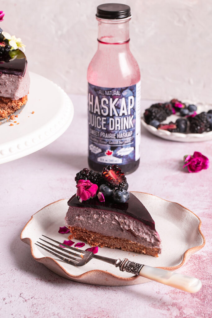 a slice of haskap berry cheesecake with a bottle of haskap juice in the background