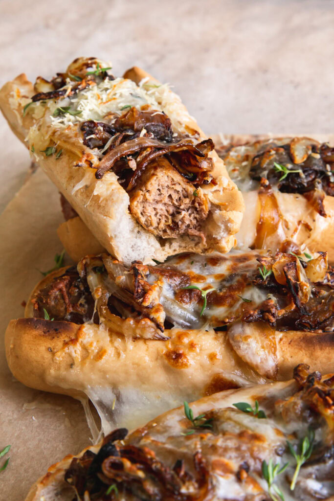 close up shot of vegan French onion brats, one with a bite taken out of it