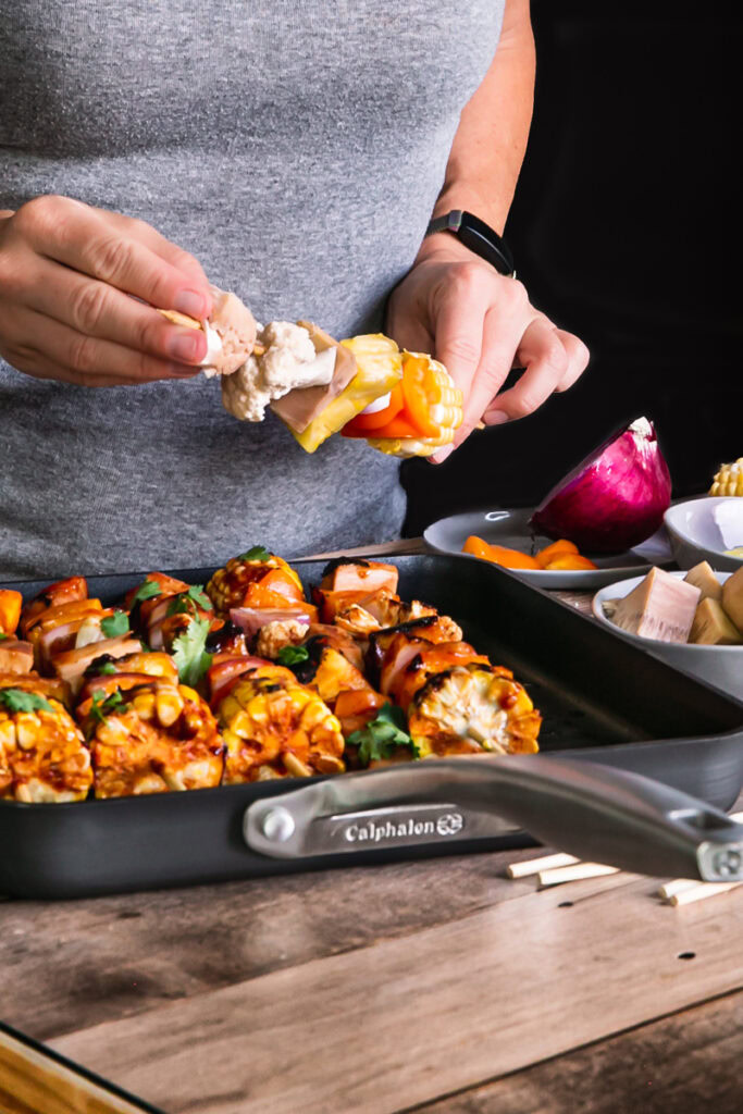 action shot of me placing the food on a kabob stick with the Calphalon grill pan on the table in front of me and the ingredients beside me