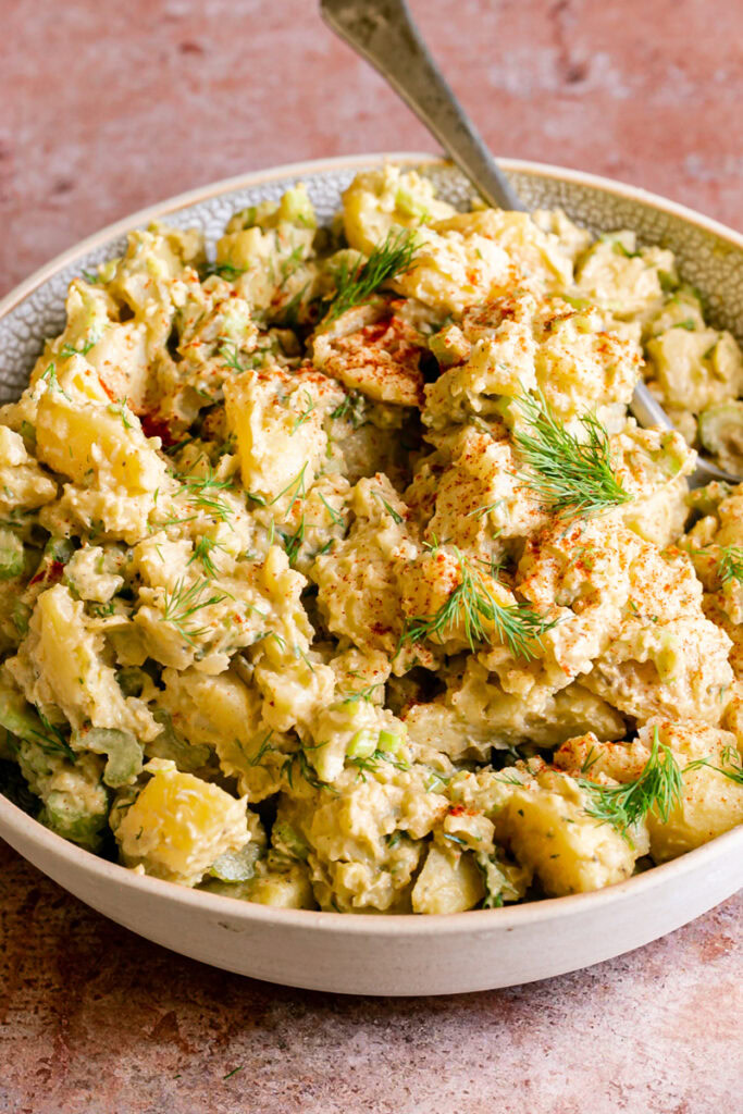 3/4 view of a bowl of smoked paprika dill potato salad with a spoon in it