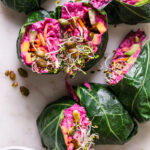 beet hummus veggie collard wraps cut in half with a bowl of beet hummus beside it