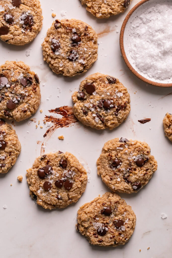 flourless salted tahini chocolate chip cookies laid out with a plate of salt beside it
