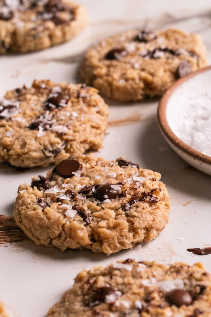 3/4 view of flourless salted tahini chocolate chip cookies with a plate of salt 