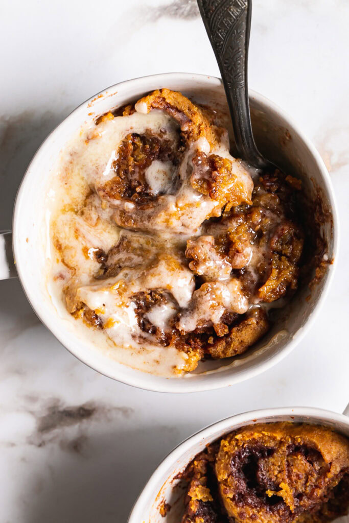 one full frame mug of pumpkin cinnamon roll mug cake and another mug peeking in the corner