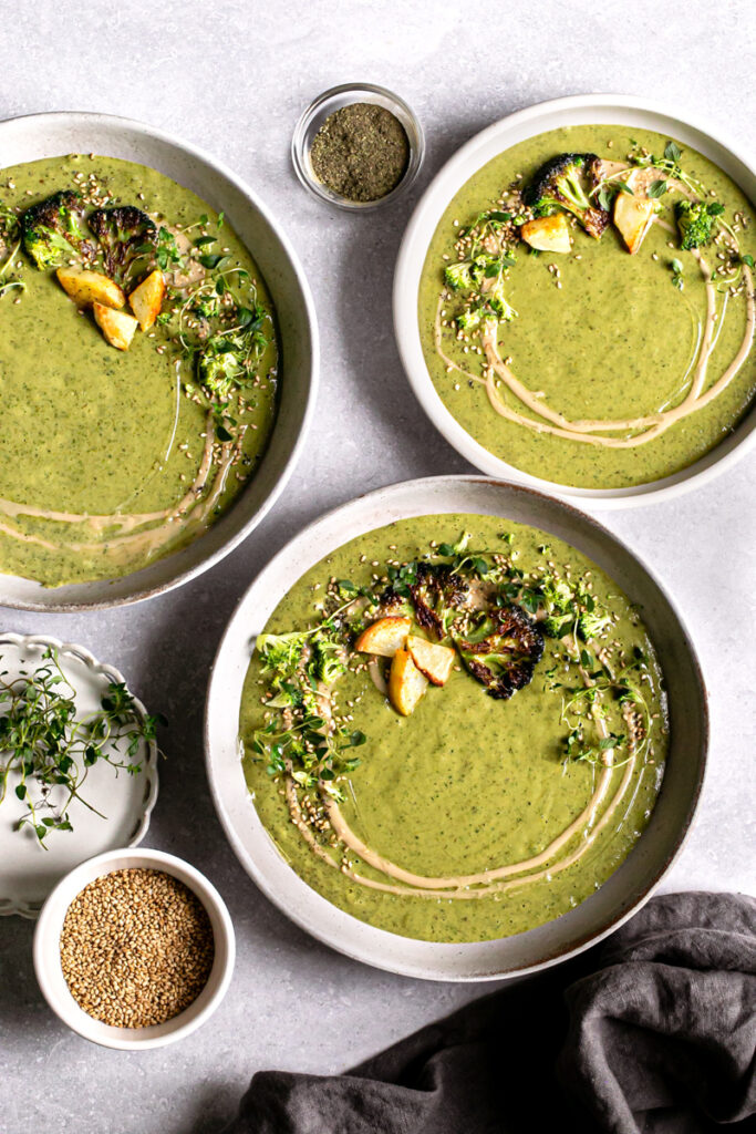 three bowls of roasted broccoli potato tahini soup garnished with broccoli and a drizzle of tahini
