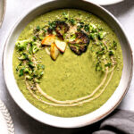 a single bowl of roasted broccoli potato tahini soup with a napkin below it