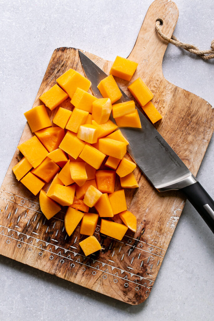 the entire butternut squash cut into chunks on a cutting board with the knife next to it