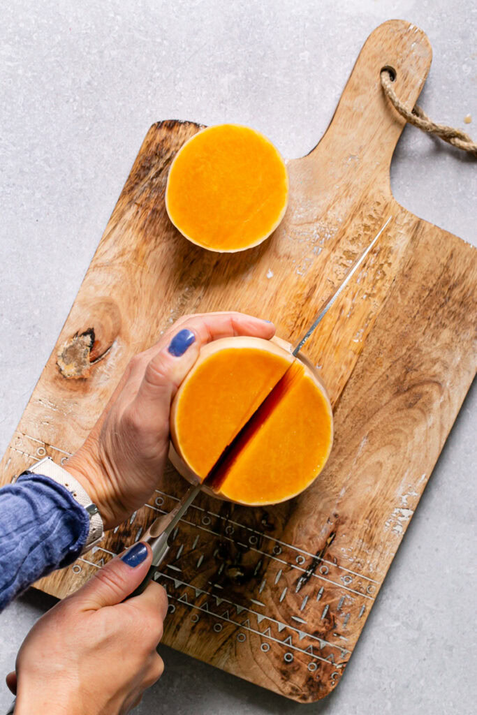 an action photo of slicing a butternut squash in half from the top down