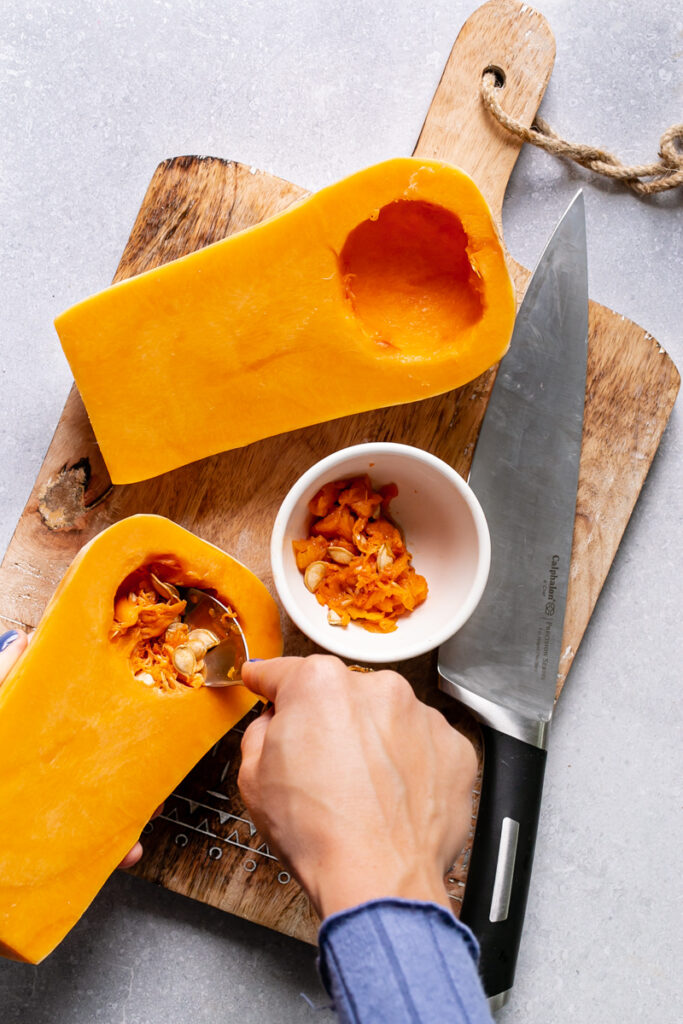 action shot of spooning out the butternut squash seeds with the Calphalon knife on the cutting board next to it