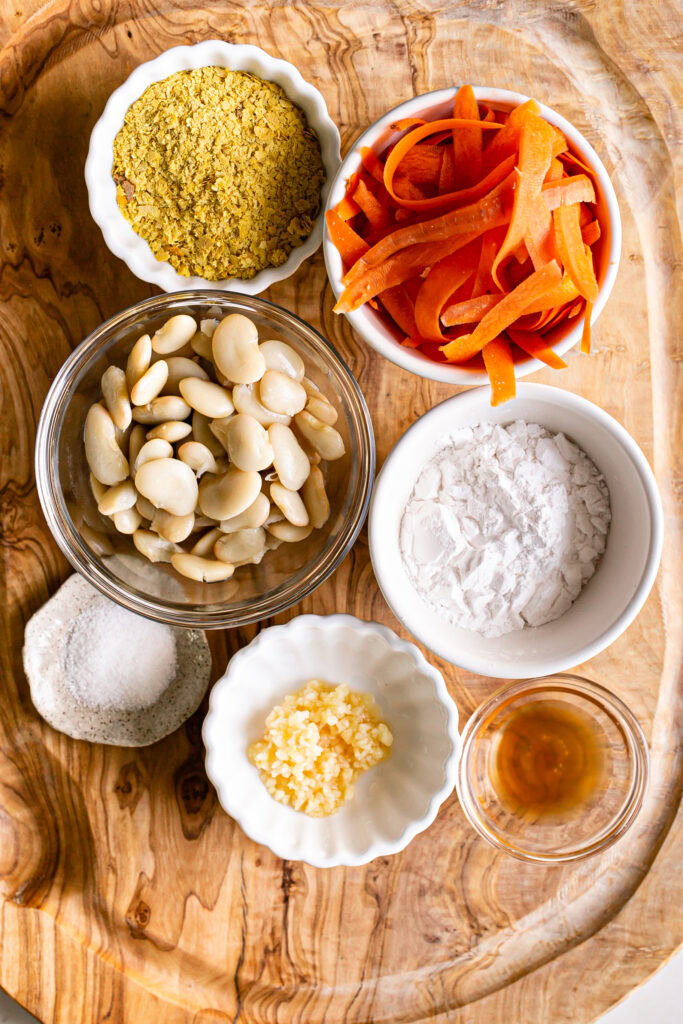 all of the ingredients to make the vegan nacho cheese sauce in bowls laid out on a wooden cutting board