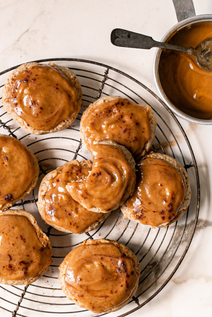 caramel apple cider cookies on a round wire baking rack topped with caramel with a saucepan of caramel beside it
