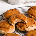 3/4 view of caramel apple cider cookies, one with a bite taken out of it and a saucepan of caramel in the background