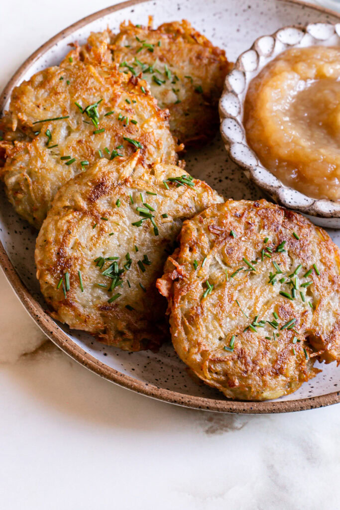 a close up 3/4 view of Gluten-Free Vegan Potato Pancakes on a plate with a side of applesauce