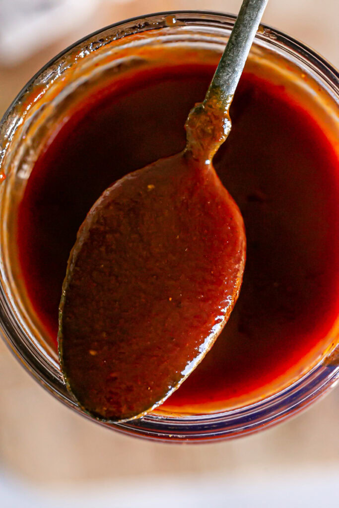 closeup overhead shot of the spoon with bbq sauce on it resting on the opening of the jar of Gluten-free Vegan Pumpkin BBQ Sauce